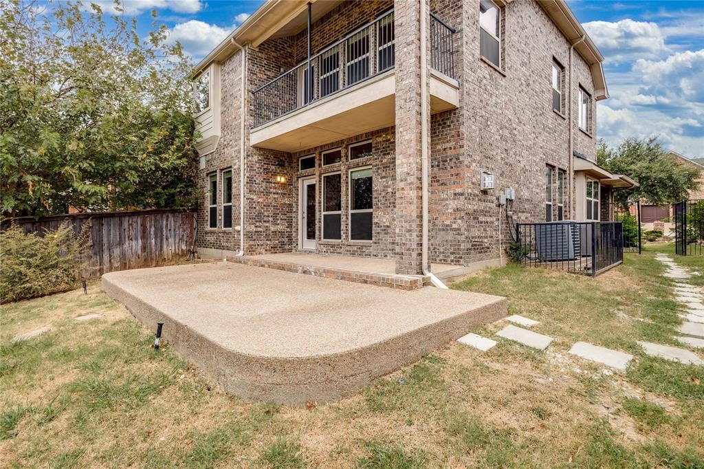 1014 Kaylie Street, Grand Prairie, TX 75052 Two-story brick exterior with an upper-level balcony featuring wrought iron railing, a ground-level concrete patio, and a fenced yard with stepping stones