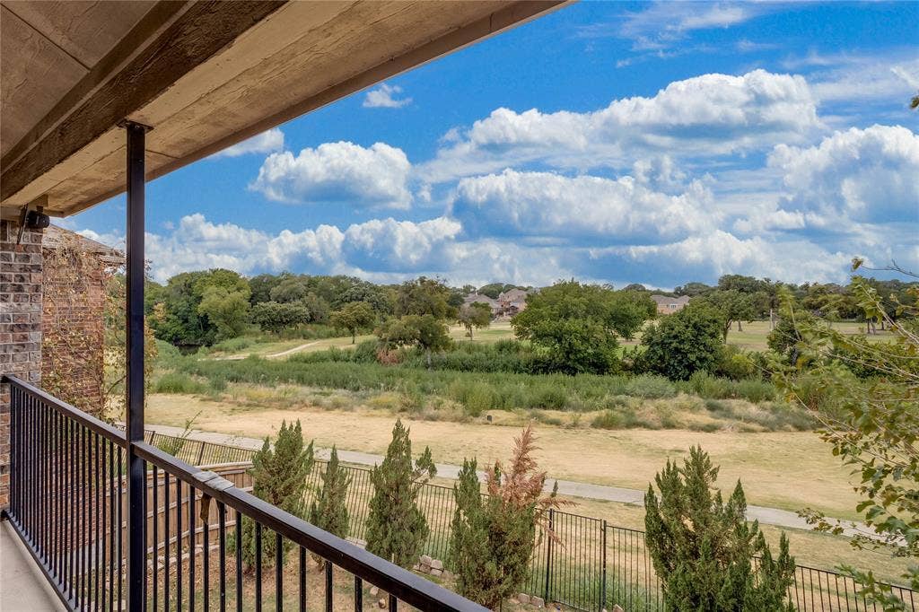 1014 Kaylie Street, Grand Prairie, TX 75052 Covered balcony featuring black metal railings and brick exterior, overlooking a landscape of mature trees and open terrain
