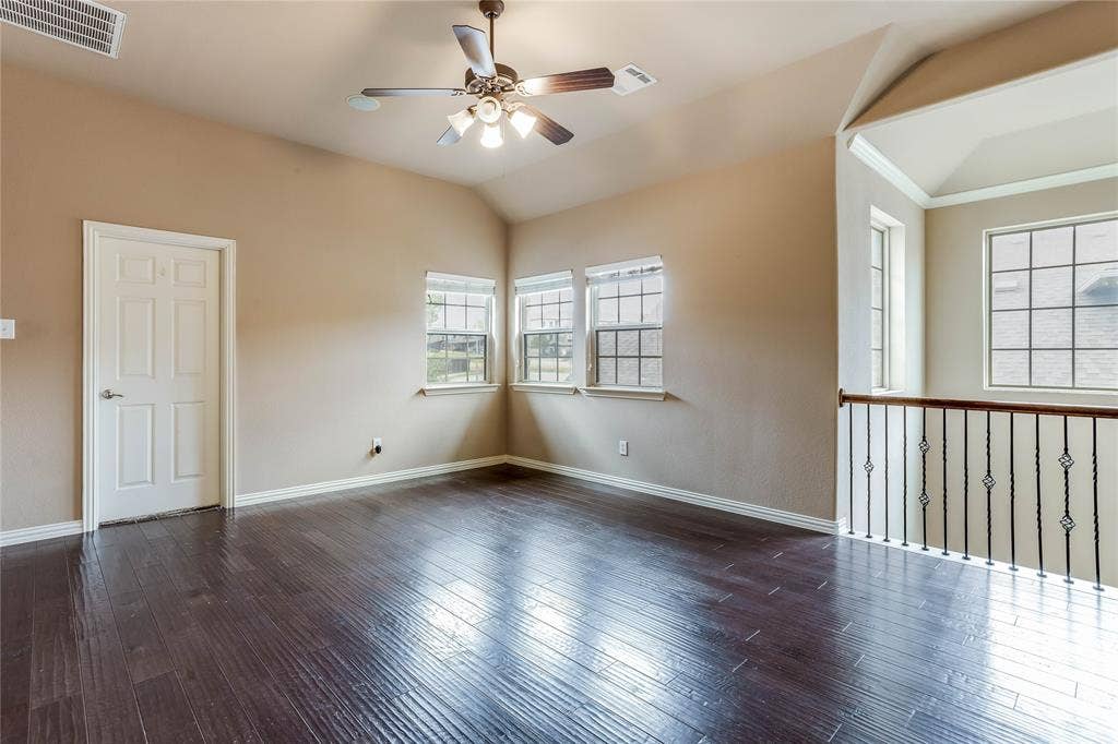 1014 Kaylie Street, Grand Prairie, TX 75052 Vaulted ceiling with a ceiling fan, three windows, wood-finish flooring, and an open railing with decorative metal spindles