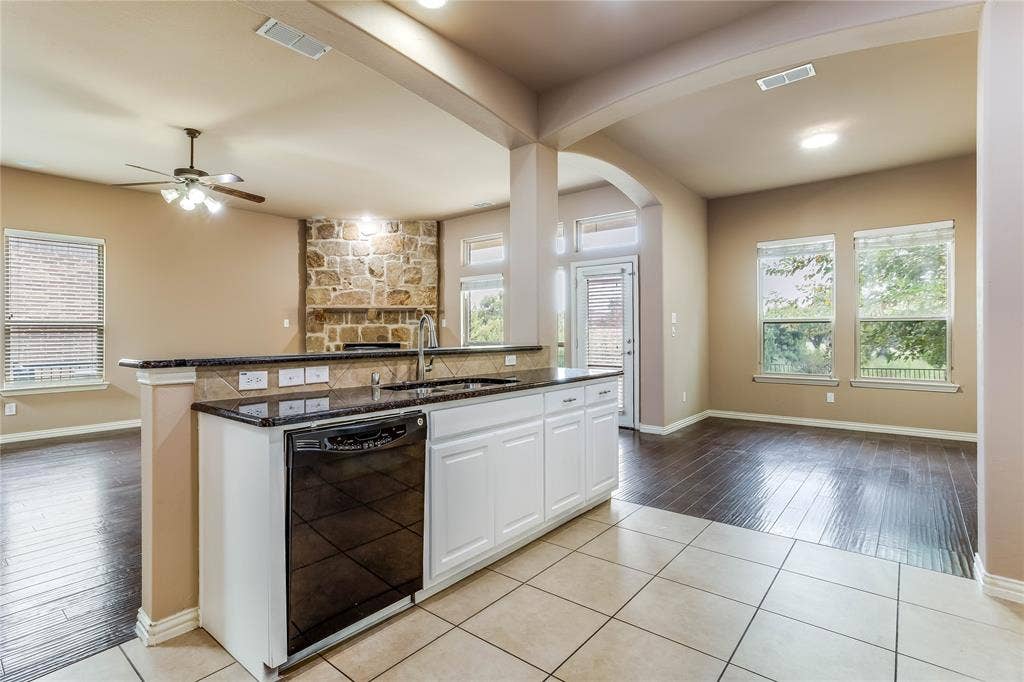 1014 Kaylie Street, Grand Prairie, TX 75052 Open-concept kitchen featuring an island with a breakfast bar, white cabinetry, a black dishwasher, and dark stone-finish countertops