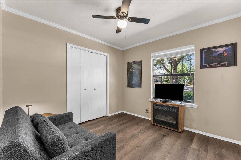 261 Oakview Circle, Waco, TX 76705 Wood-finish flooring, white bi-fold closet doors, ceiling fan with integrated lighting, white crown molding, and a window with exterior tree scenery