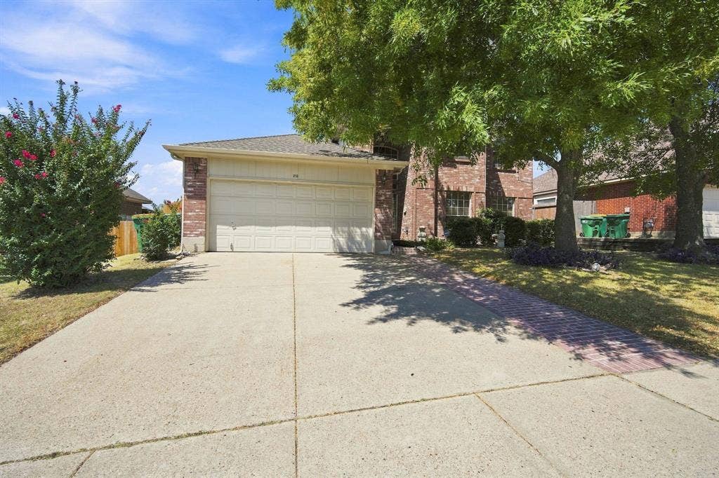 Brick facade with an integrated two-car garage, concrete driveway, and mature landscaping