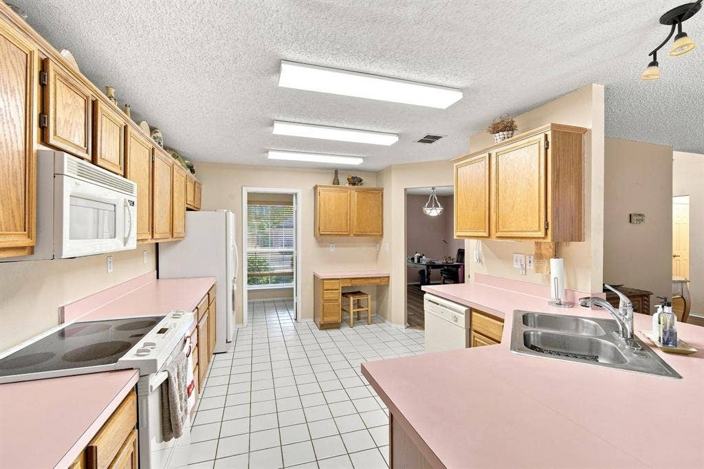Kitchen featuring light wood cabinetry, pink countertops, white tile flooring, and a stainless steel double basin sink