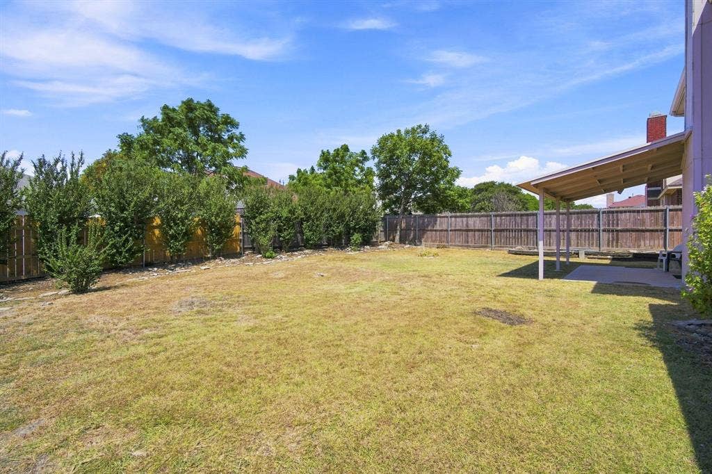 Spacious backyard featuring a covered patio, wood privacy fence, and mature perimeter landscaping