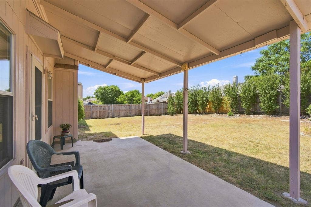 Expansive covered patio with concrete flooring, supported by multiple posts, opening to a large backyard with a privacy fence