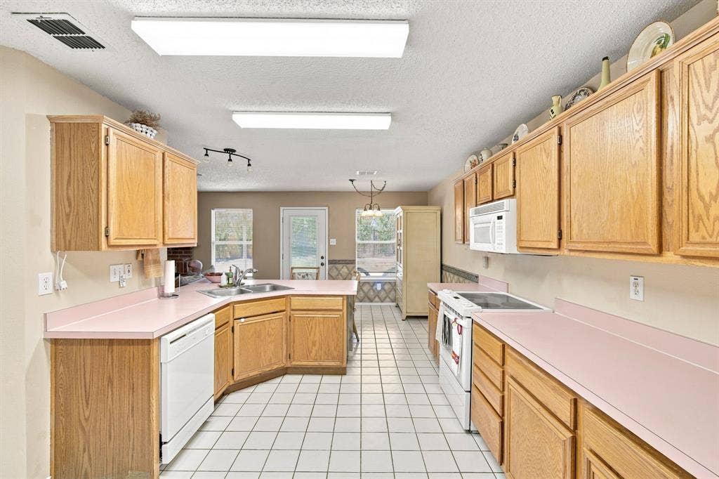 Expansive kitchen featuring wood-finish cabinetry, white tile flooring, and light-colored countertops