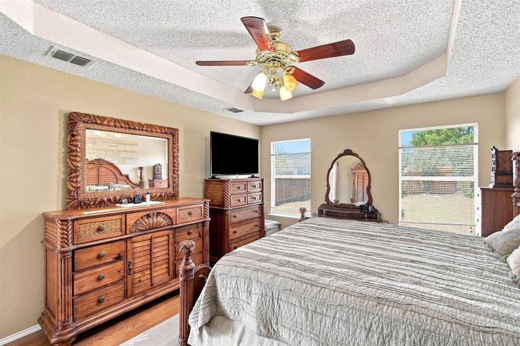 Tray ceiling with a ceiling fan, dual windows, and wood-finish flooring