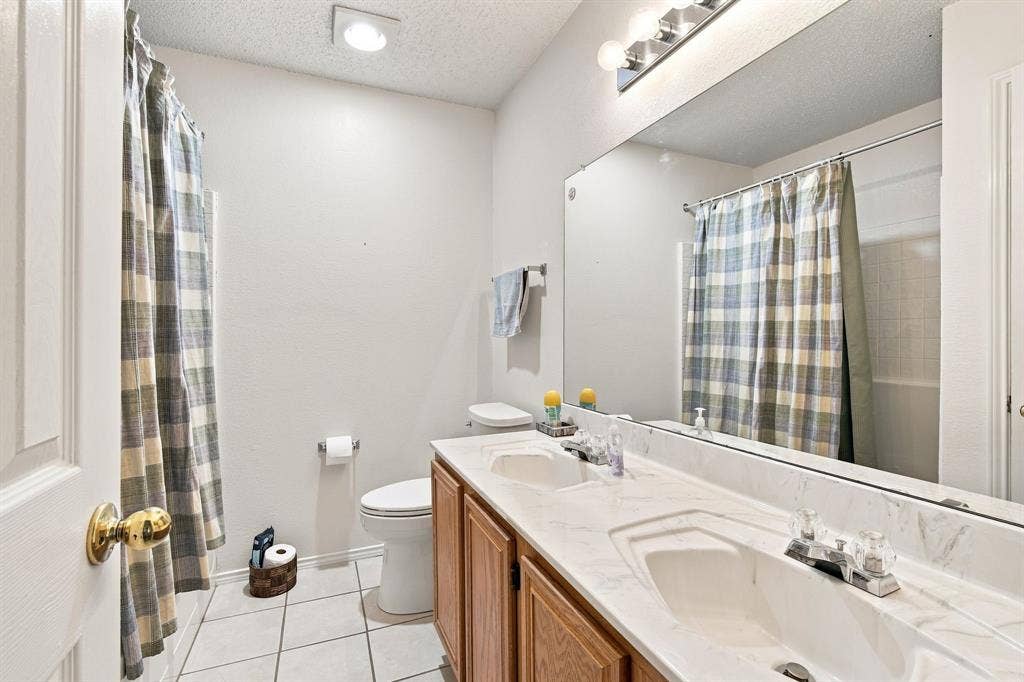 Dual vanity with integrated sinks, wood-finish cabinetry, a large wall-mounted mirror, and tile flooring