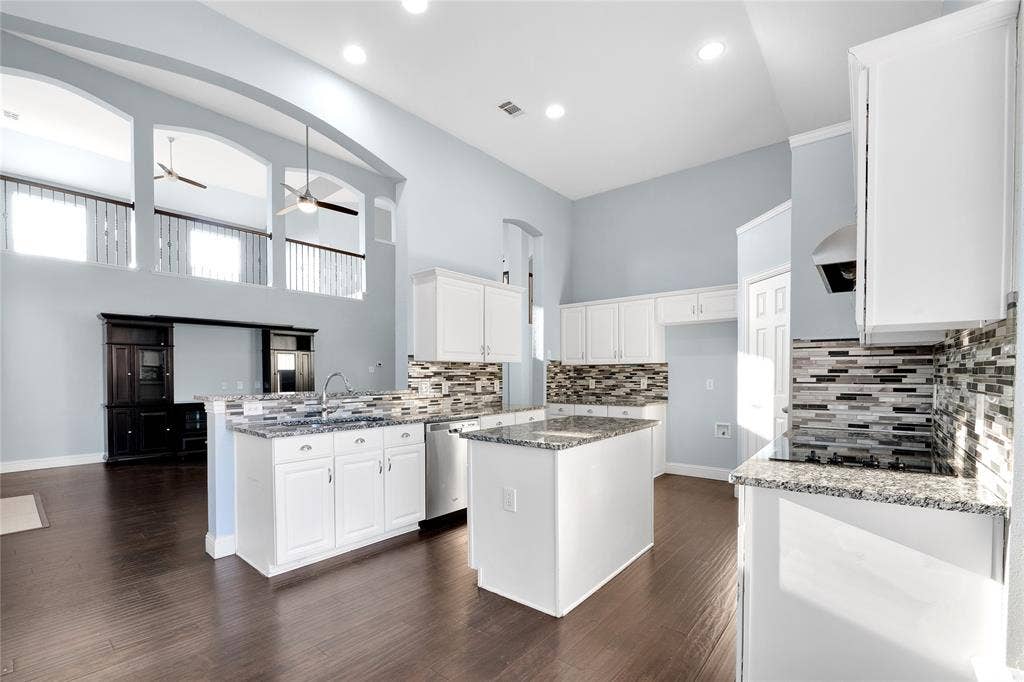 2106 Hillside Drive, Rowlett, TX 75088 Bright, open kitchen featuring granite countertops, white cabinetry, a center island, modern backsplash, and an open view into the living area.