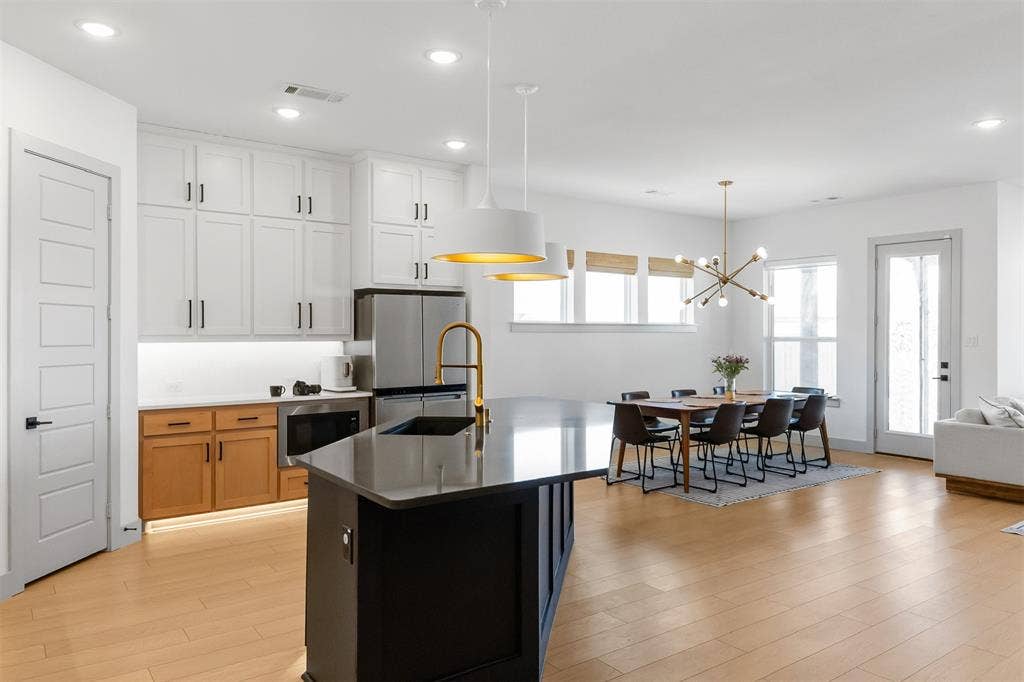 2308 Clancy Drive, Northlake, TX 76247 Open-concept kitchen and dining area featuring light wood-finish flooring, a kitchen island with a dark countertop, white upper cabinetry, and a dining area with multiple windows