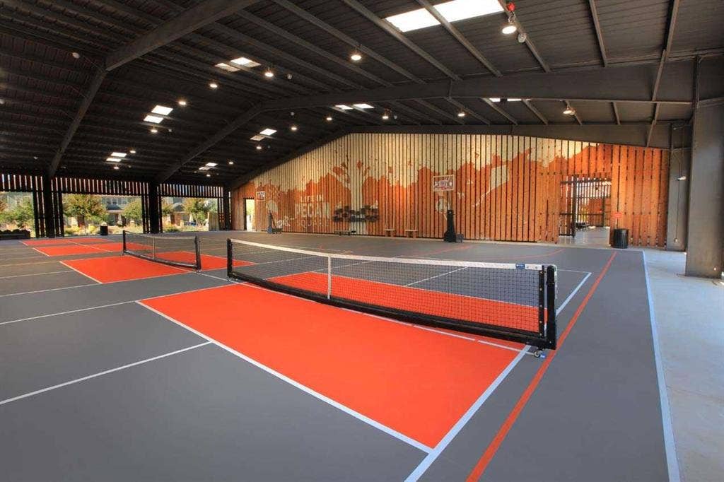 2308 Clancy Drive, Northlake, TX 76247 Indoor recreational court with multiple painted playing areas, a high vaulted ceiling with skylights, extensive wood-paneled wall accents, and an open-air architectural design
