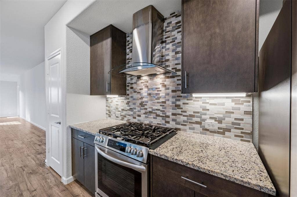 4425 Ridgehurst Lane, Fort Worth, TX 76036 Stainless steel range with gas cooktop, granite countertops, tile backsplash, dark wood-finish cabinetry, and under-cabinet lighting