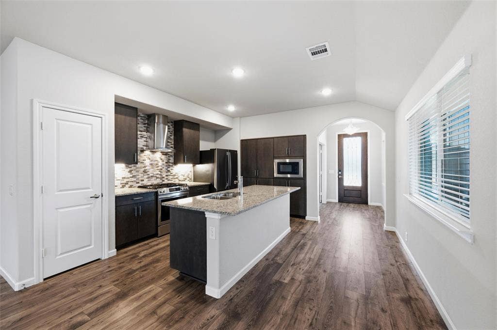 4425 Ridgehurst Lane, Fort Worth, TX 76036 Kitchen featuring wood-finish flooring, dark wood cabinetry, a mosaic tile backsplash, and a center island with a light-colored countertop