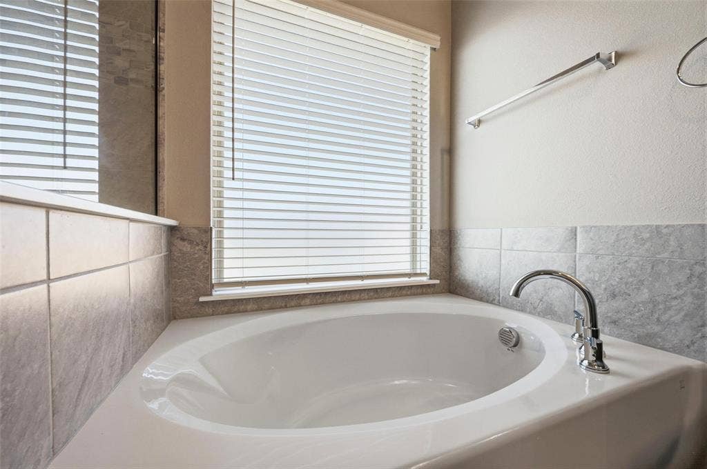 4425 Ridgehurst Lane, Fort Worth, TX 76036 Corner soaking tub with chrome fixtures, tiled surround, and window with blinds