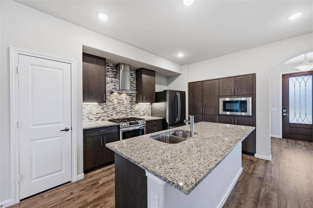 4425 Ridgehurst Lane, Fort Worth, TX 76036 Modern kitchen featuring dark cabinetry with stainless steel appliances, a mosaic tile backsplash, and a spacious granite-topped island with white base cabinetry
