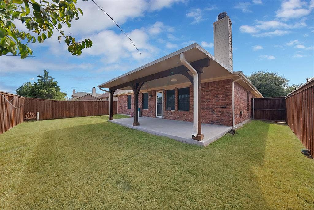Expansive backyard featuring a manicured lawn, full privacy fencing, and a covered concrete patio with robust support beams