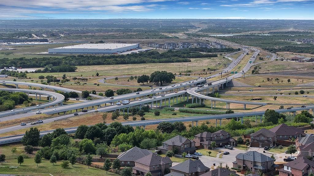 Aerial perspective showcasing residential development, extensive roadway infrastructure, and distant commercial buildings