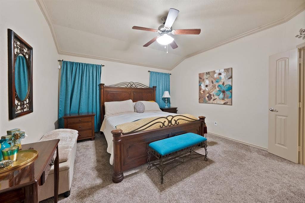 Vaulted ceiling with crown molding, ceiling fan, and light-colored carpet flooring