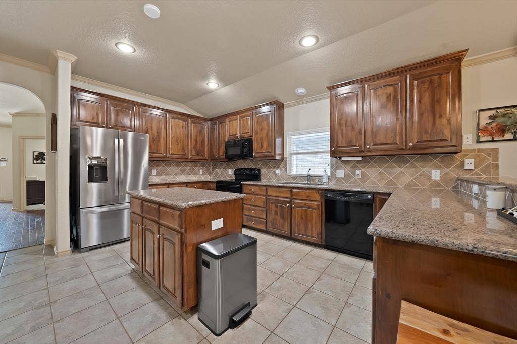 Kitchen featuring wood cabinetry, granite countertops, tile flooring, and a tile backsplash