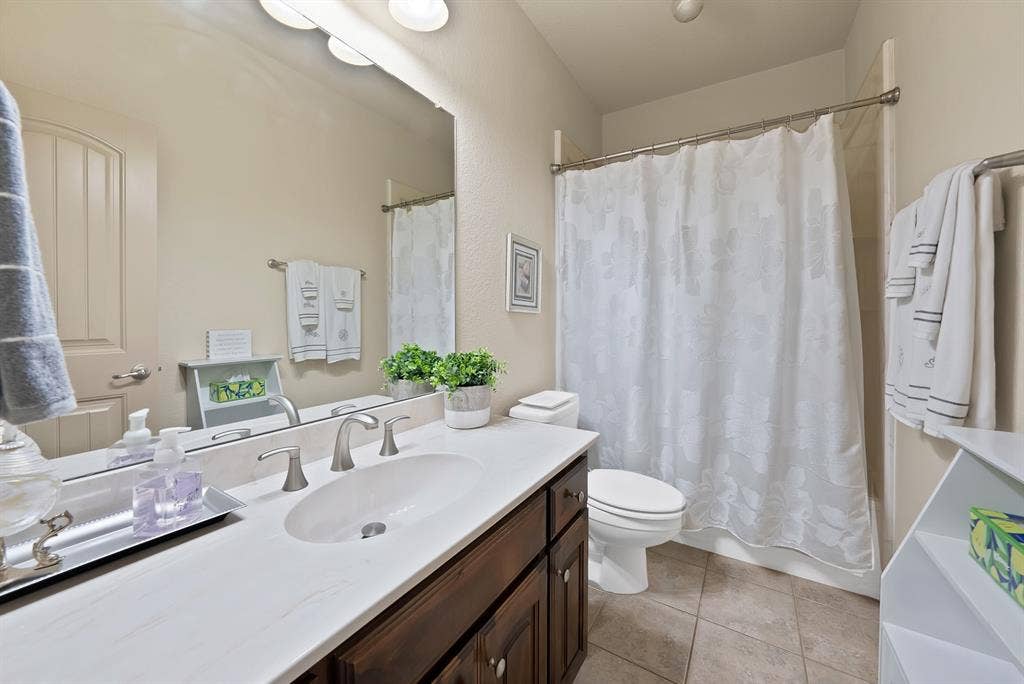 Vanity with an integrated sink, brushed nickel fixtures, a full-width mirror, and a combination shower-tub with a privacy curtain