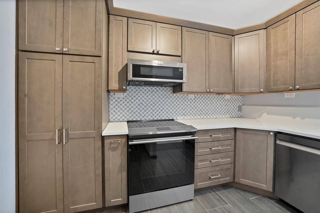 330 Las Colinas Boulevard E, #338, Irving, TX 75039 Kitchen featuring wood-finish cabinetry, stainless steel appliances, patterned tile backsplash, white countertops, and tile flooring
