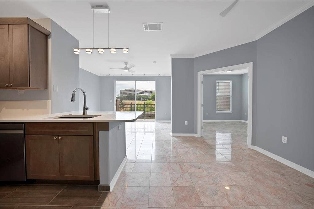 330 Las Colinas Boulevard E, #338, Irving, TX 75039 Kitchen island with a built-in sink and gooseneck faucet, stainless steel dishwasher, wood-finish cabinetry, and light-toned countertop