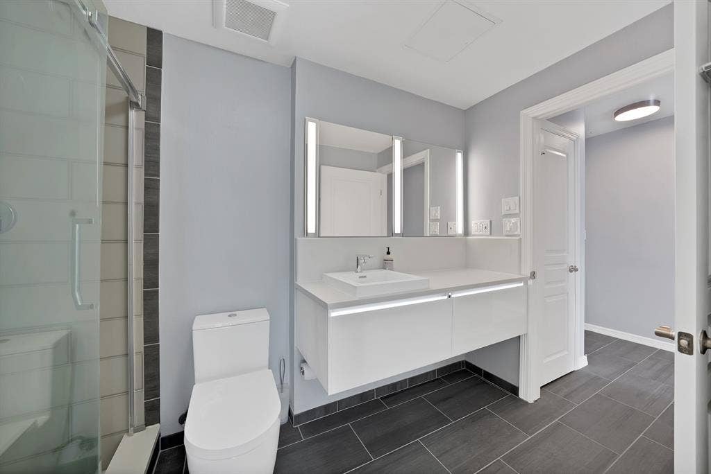 330 Las Colinas Boulevard E, #338, Irving, TX 75039 Glass-enclosed shower with tiled surround, floating vanity with integrated lighting, rectangular vessel sink, illuminated mirrored medicine cabinets, and dark-toned floor tiling