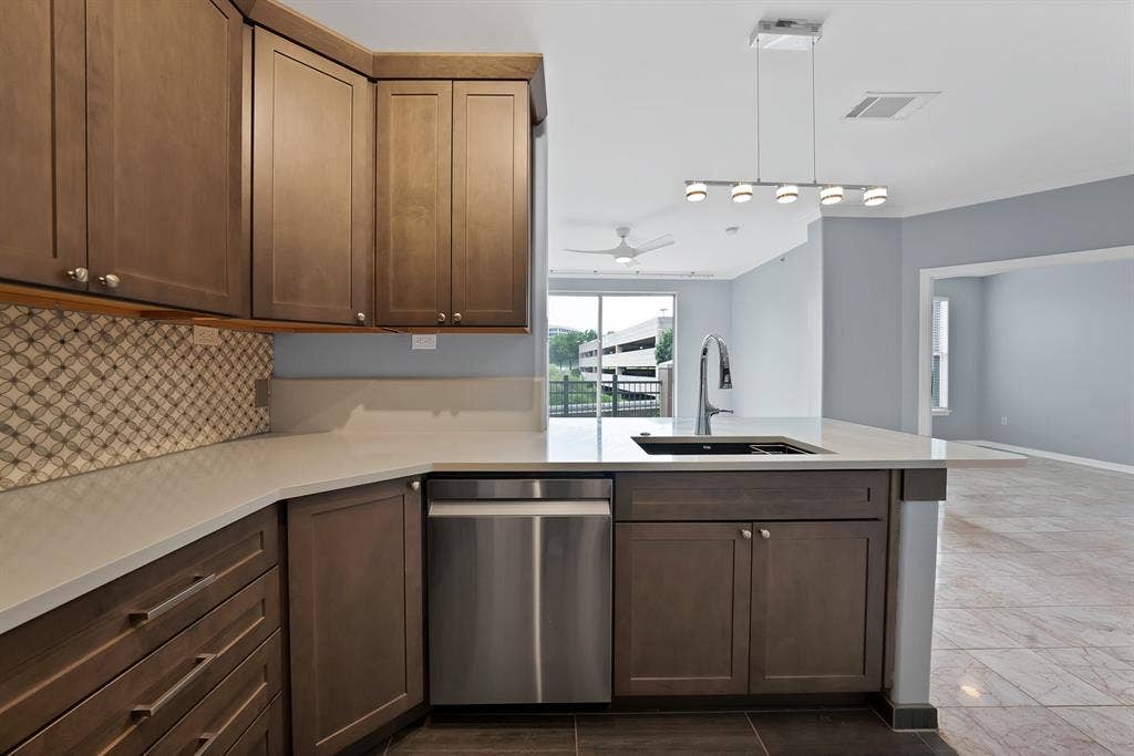 330 Las Colinas Boulevard E, #338, Irving, TX 75039 Full kitchen with wood cabinetry, stainless steel dishwasher, an integrated sink with a gooseneck faucet, light-toned countertops, and a patterned tile backsplash