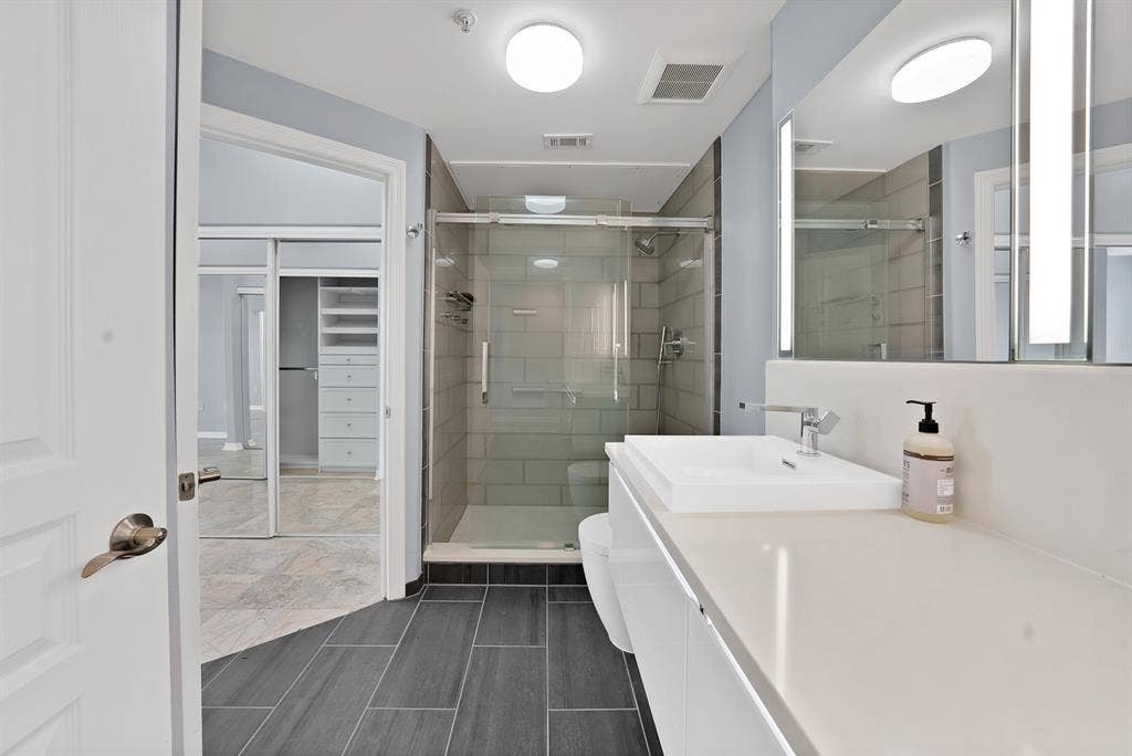 330 Las Colinas Boulevard E, #338, Irving, TX 75039 Contemporary bathroom with a glass-enclosed shower, integrated sink vanity, light-toned countertop, and dark rectangular floor tiles