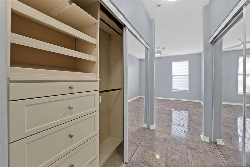 330 Las Colinas Boulevard E, #338, Irving, TX 75039 Built-in closet organization system with shelving and drawers, mirrored sliding closet doors, ceiling fan, and tile flooring