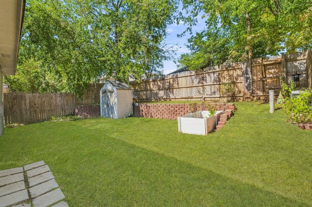 6913 Chaco Trail, Fort Worth, TX 76137 Expansive grassy yard with wood fencing, a storage shed, and a raised garden bed with brick retaining walls