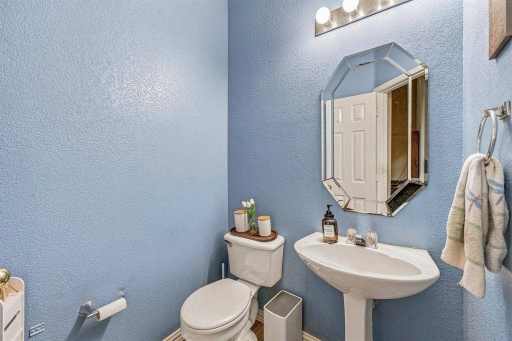 6913 Chaco Trail, Fort Worth, TX 76137 Pedestal sink with chrome-finish faucet, octagonal mirror, vanity bar lighting, and a white toilet