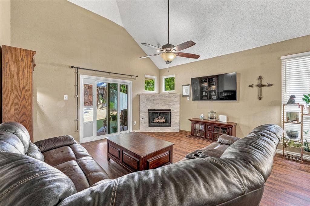 6913 Chaco Trail, Fort Worth, TX 76137 Vaulted ceiling, wood-finish flooring, stone-clad fireplace with hearth, ceiling fan, and sliding glass door