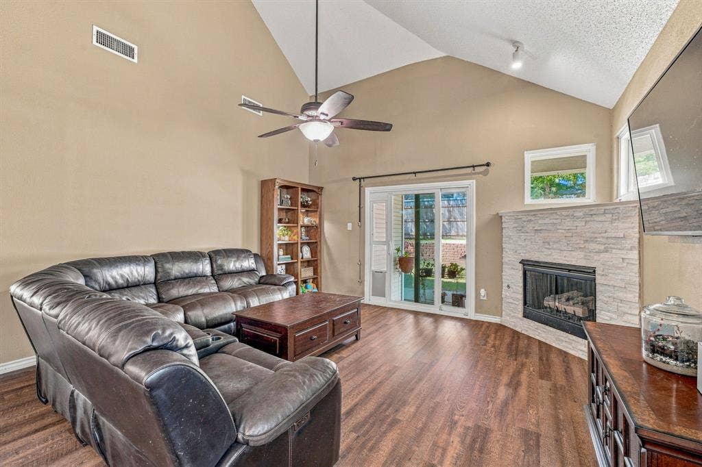 6913 Chaco Trail, Fort Worth, TX 76137 Vaulted ceiling with an installed ceiling fan, wood-finish flooring, a fireplace with a stacked stone surround, and sliding glass doors