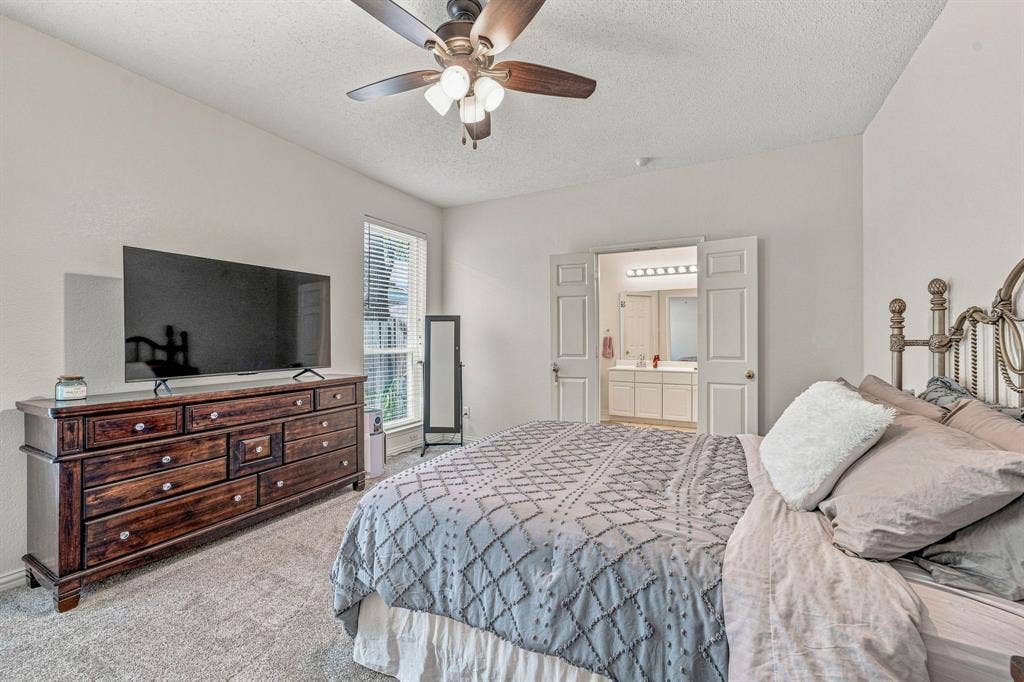 6913 Chaco Trail, Fort Worth, TX 76137 Neutral wall paint, carpeted flooring, window with blinds, ceiling fan with integrated lighting, and double-door entry to a bathroom