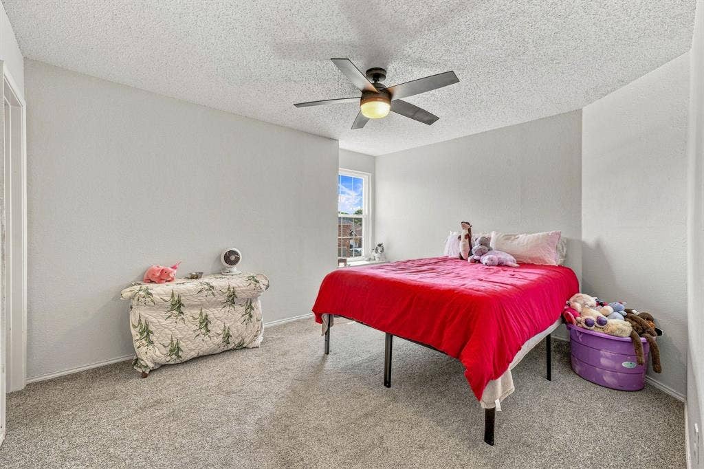 6913 Chaco Trail, Fort Worth, TX 76137 Light gray wall paint, textured ceiling, ceiling fan with integrated lighting, window with exterior building visibility, and gray carpet