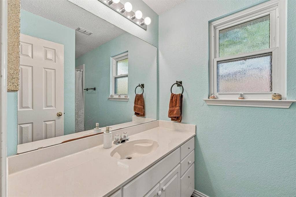 6913 Chaco Trail, Fort Worth, TX 76137 White vanity with integrated sink, full-width mirror, and a multi-bulb light fixture