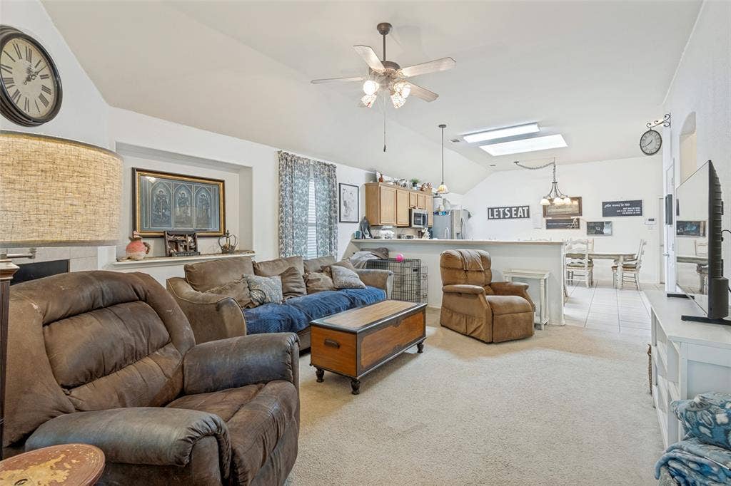 2118 Hanakoa Falls Drive, Anna, TX 75409 Vaulted ceiling with a ceiling fan, recessed fireplace, built-in shelving, kitchen with wood cabinetry, and a skylight