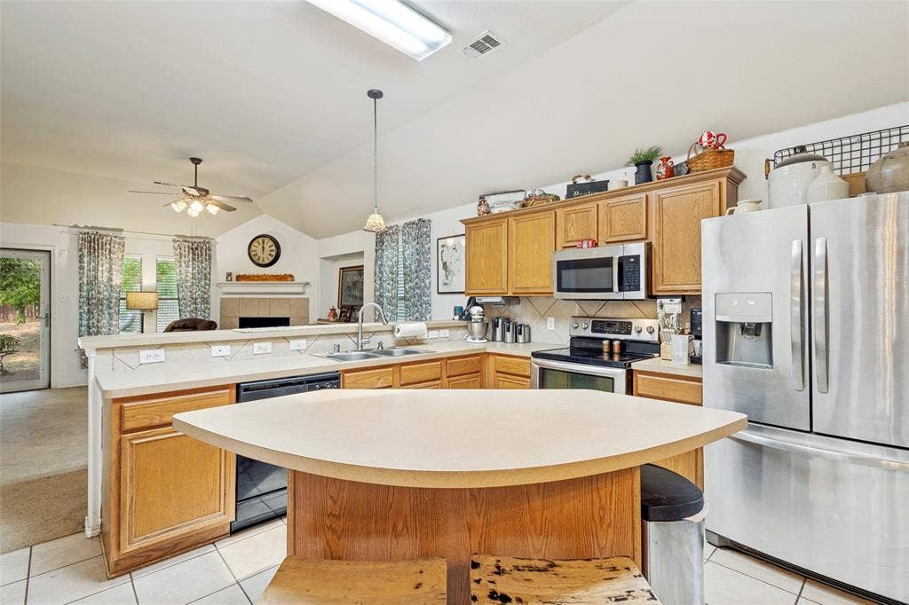 2118 Hanakoa Falls Drive, Anna, TX 75409 Kitchen featuring wood cabinetry, stainless steel appliances, a corner sink with a stainless steel faucet, a breakfast bar, and tile flooring