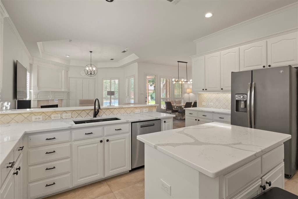 White cabinetry with black hardware, white countertops, tile backsplash, built-in stainless steel appliances, and a central island