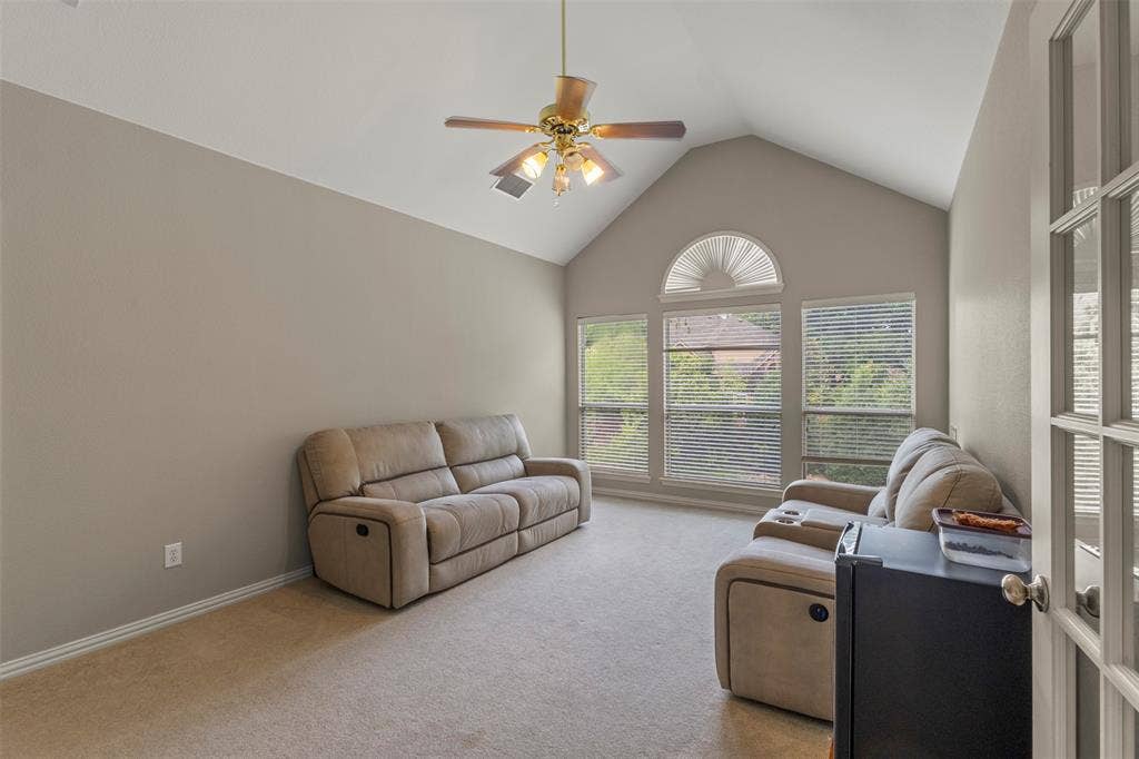 Vaulted ceiling with an illuminated ceiling fan, a series of windows, and a glass-paneled door