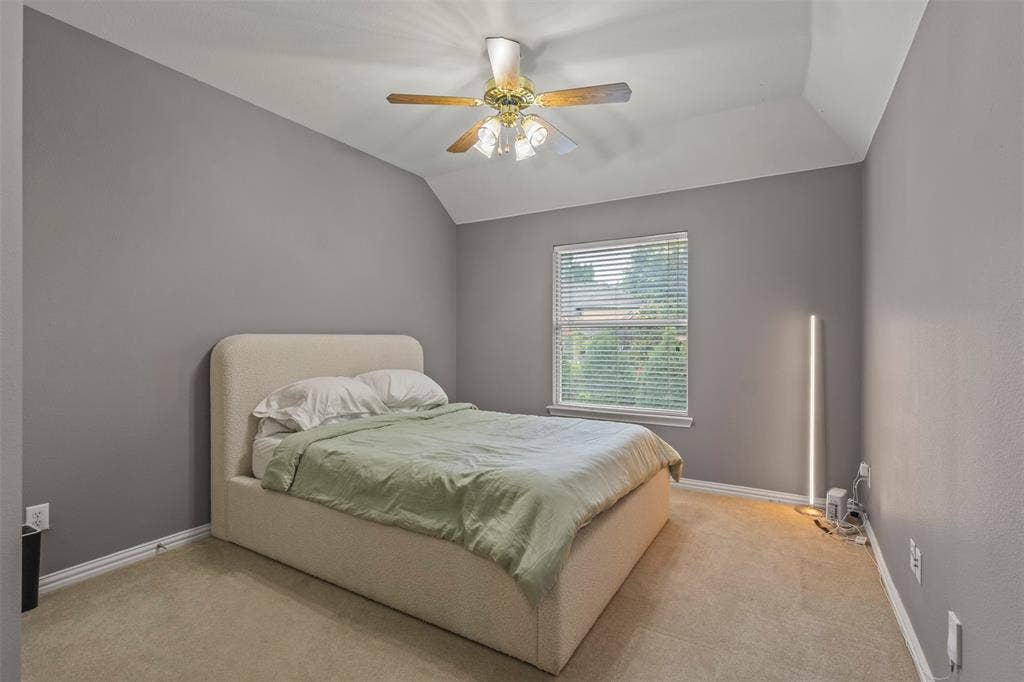 Carpeted room featuring a window with blinds, ceiling fan with lighting, and vaulted ceiling