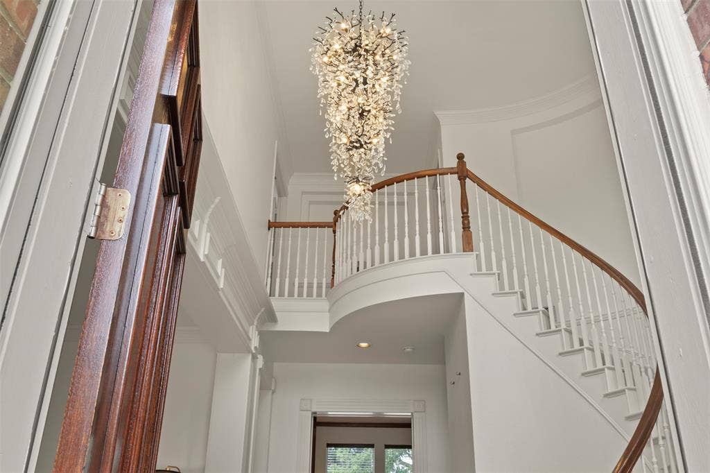 Stunning two-story foyer showcasing a curved staircase with wood-finish railings and white balusters, accented by a dramatic crystal chandelier suspended from the ceiling