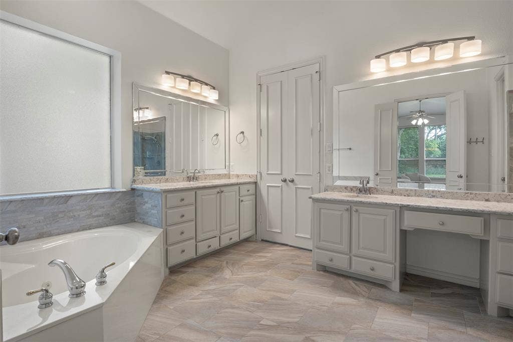 Dual vanities with integrated sinks and white cabinetry, a built-in soaking tub with chrome fixtures, and wood-finish flooring