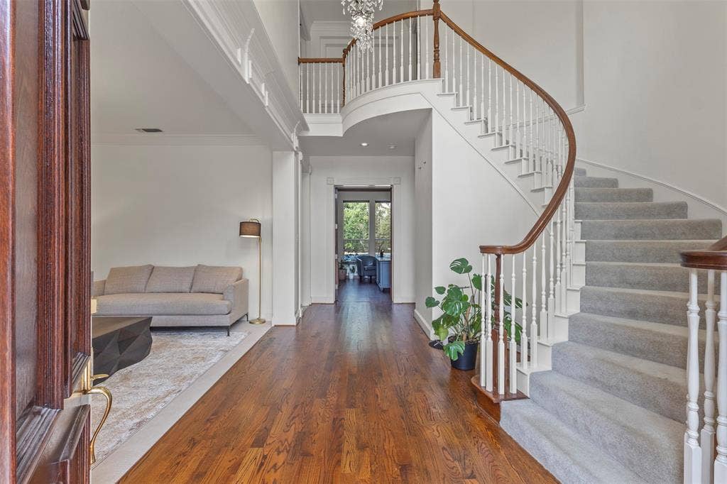 Wood-finish flooring with a curved staircase featuring carpeted treads, white balusters, and a rich wood handrail