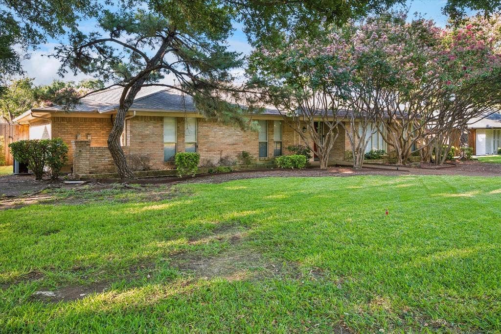 4108 Myerwood Lane, Dallas, TX 75244 Single-story brick home with a manicured lawn and lush, tree-shaded landscaping.