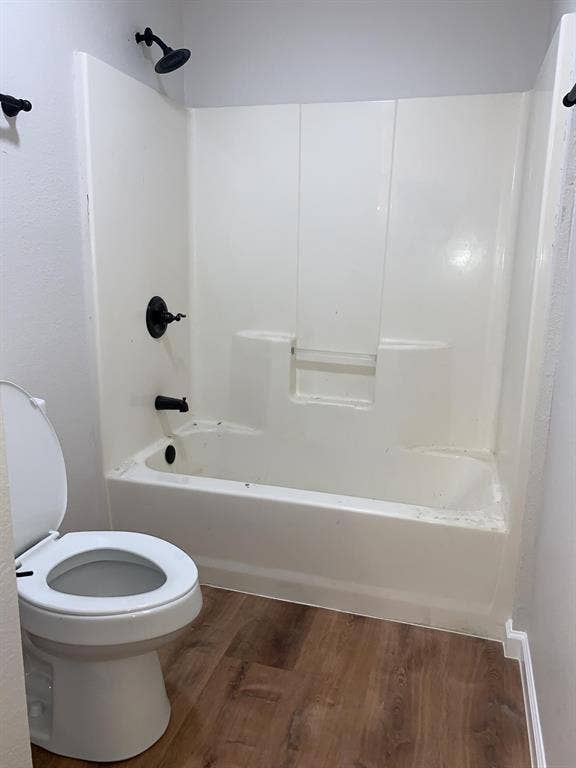 120 Plumthicket Lane, Trinidad, TX 75163 White toilet with a coordinated shower and tub combination featuring matte black fixtures, set on wood-finish flooring