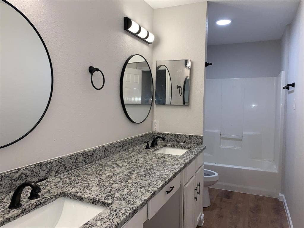 120 Plumthicket Lane, Trinidad, TX 75163 Dual undermount sinks with black fixtures, granite-look countertops, white cabinetry with black hardware, and wood-finish flooring