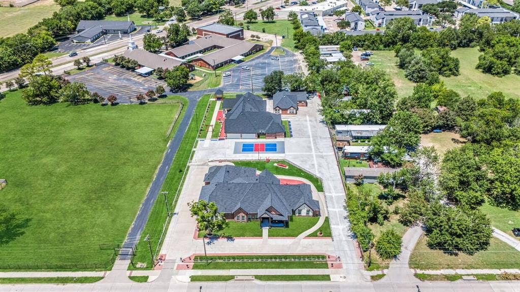 703 E Oates Road, Garland, TX 75043 Expansive property featuring multiple buildings with dark shingle roofs, substantial paved hardscaping, and distinct green spaces