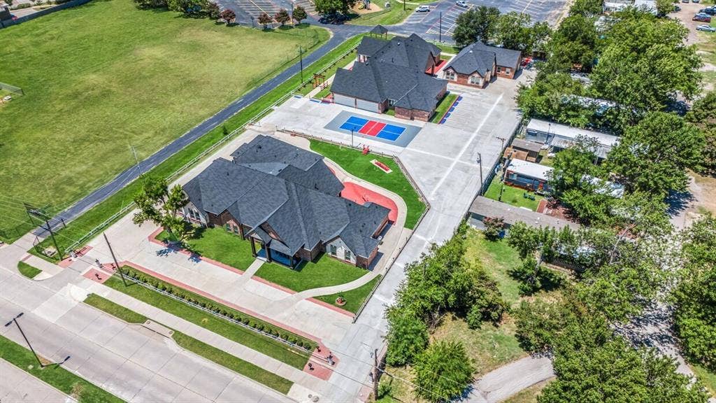 703 E Oates Road, Garland, TX 75043 Two substantial buildings with dark shingle roofs, expansive concrete paving, and a dedicated sports court